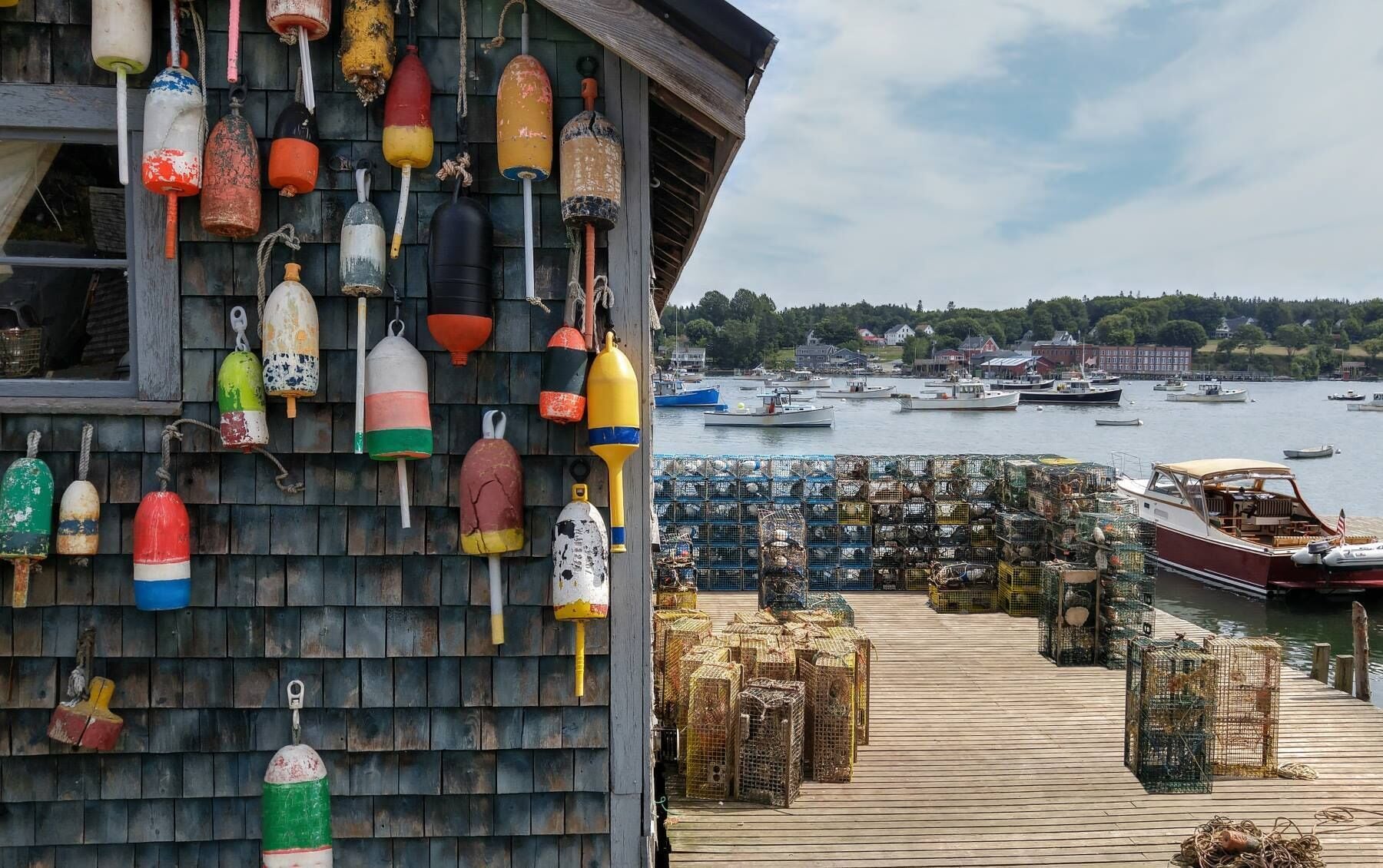 A wooden building with colorful buoys hanging on the wall and a dock with lobster traps.