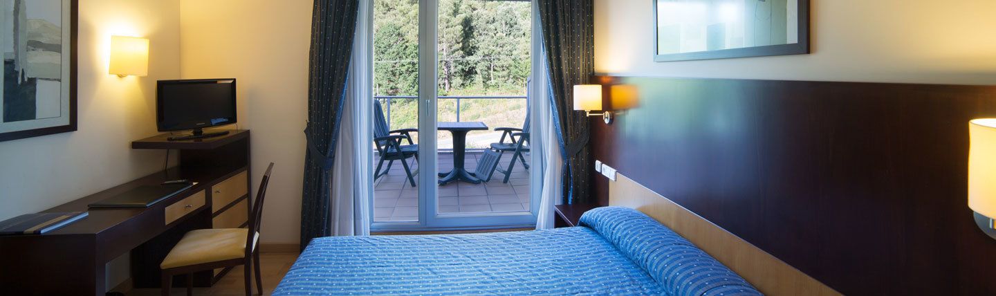 Habitación de hotel con cama, escritorio, silla y vistas al exterior a través de una puerta corrediza.