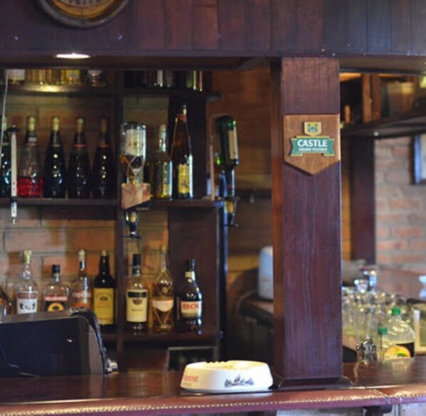 Un espace bar avec un comptoir en bois, des étagères remplies de différentes bouteilles d’alcool et un panneau indiquant « CASTLE ».