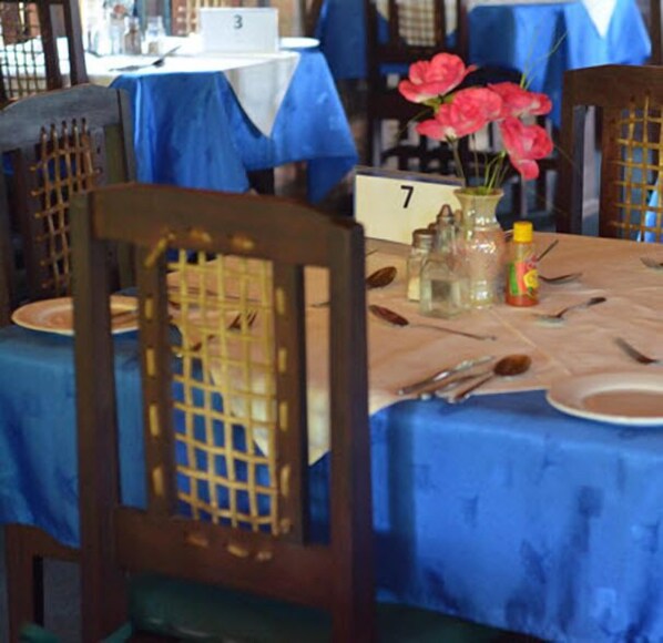 A dining table with a blue tablecloth, numbered 7, and a vase with pink flowers. - Eden Lodge Vumba (Mutare)