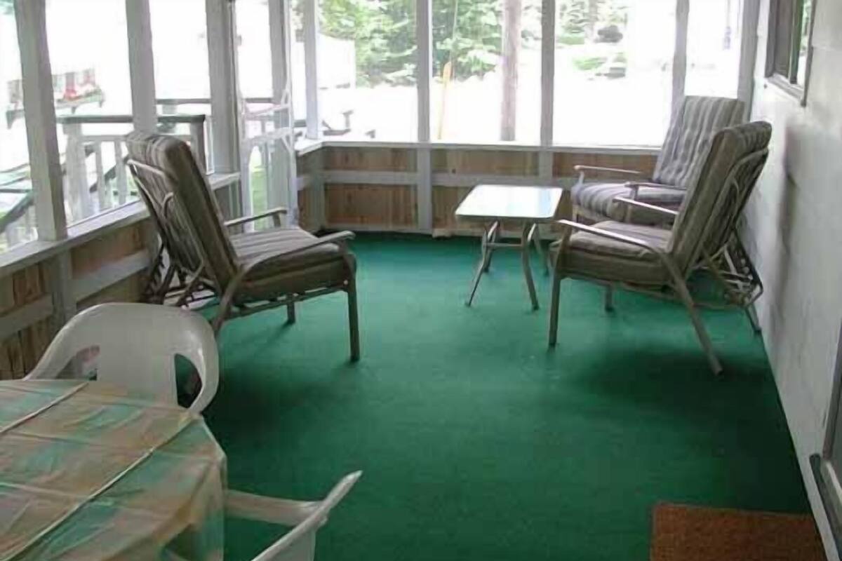 A room with a green carpet, wooden chairs, a table, and large windows.
