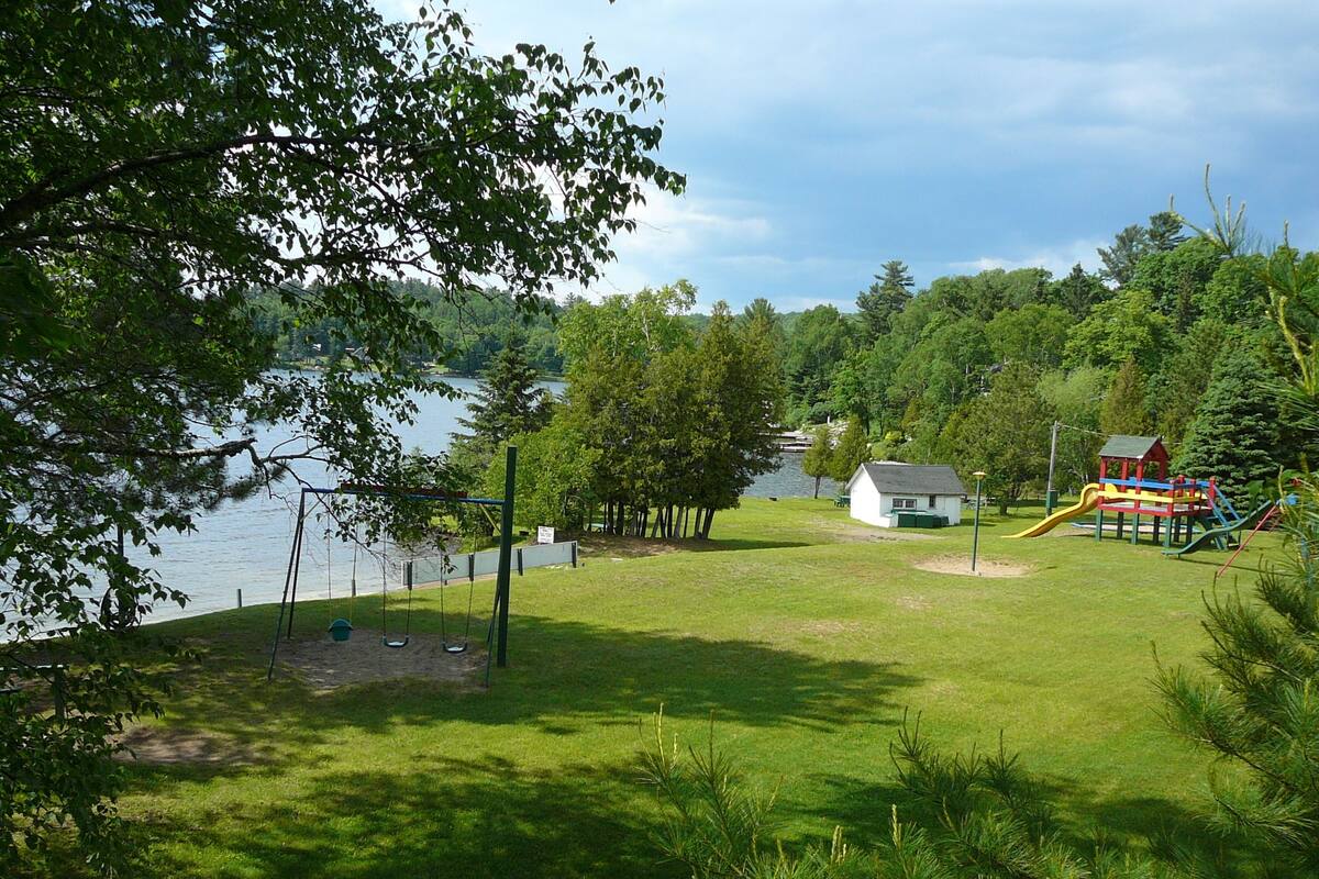A park with a playground, a small house, and a lake.