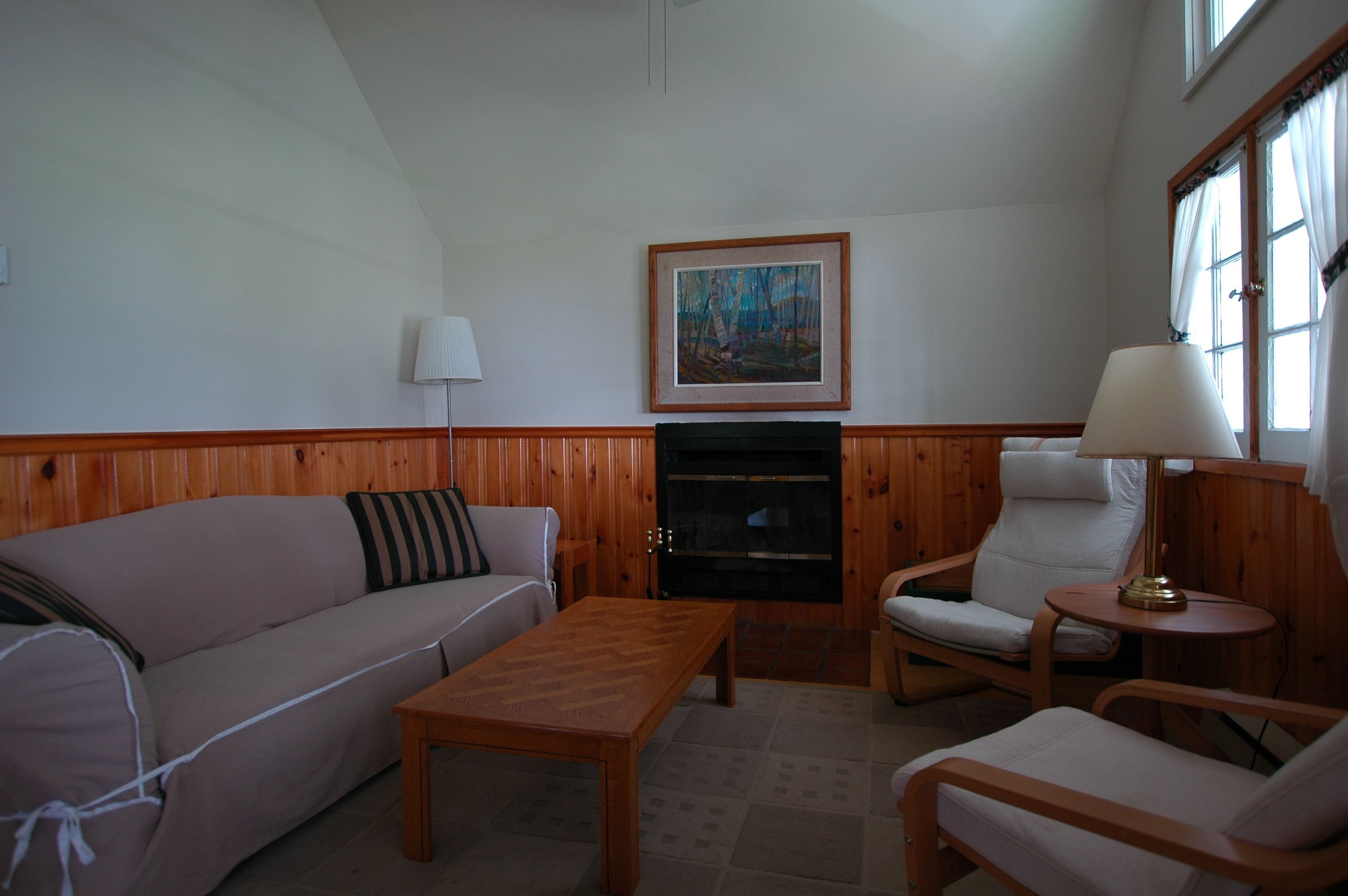 Ein gemütliches Wohnzimmer mit einer Holzwand, einem Sofa, einem Sessel, einem Couchtisch und einem Kamin.