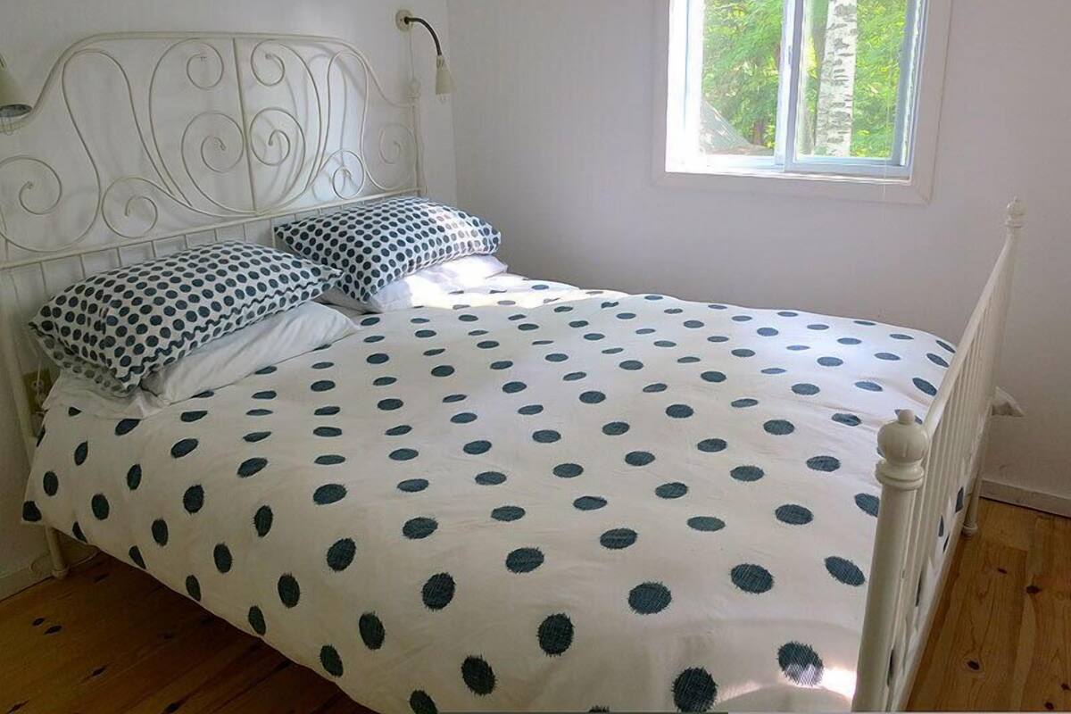 A bedroom with a white bed, polka dot bedding, a white metal headboard, and a window with a view of trees.
