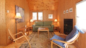 A cozy wooden cabin interior with a sofa, two rocking chairs, a small table, and a fireplace. - Birch Cliff Lodge on Baptiste Lake (Hastings Highlands)