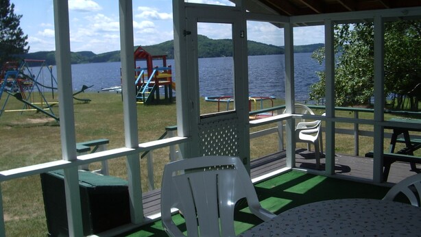 A covered outdoor area with a view of a lake, picnic tables, and playground equipment. - Birch Cliff Lodge on Baptiste Lake (Hastings Highlands)