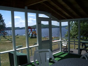 A covered outdoor area with a view of a lake, picnic tables, and playground equipment. - Birch Cliff Lodge on Baptiste Lake (Hastings Highlands)