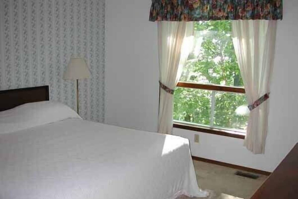 A bedroom with a bed, a window with curtains, and a lamp.