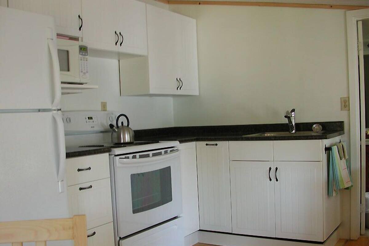 A kitchen with white cabinets, a stove, a microwave, and a kettle on the counter.