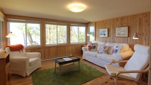 A cozy living room with a white sofa, a white armchair, a green rug, and a wooden coffee table. - Birch Cliff Lodge on Baptiste Lake (Hastings Highlands)