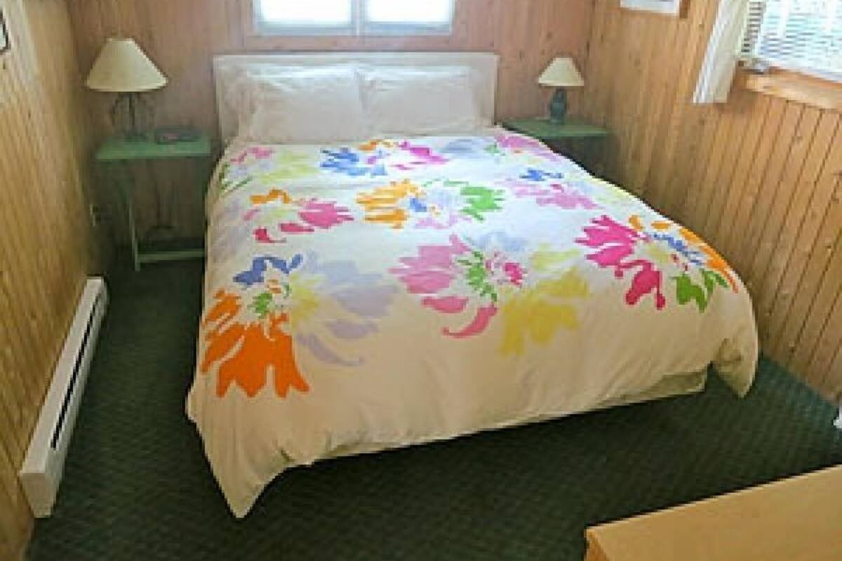A bedroom with a floral bedspread, two bedside tables with lamps, a window, and a radiator.