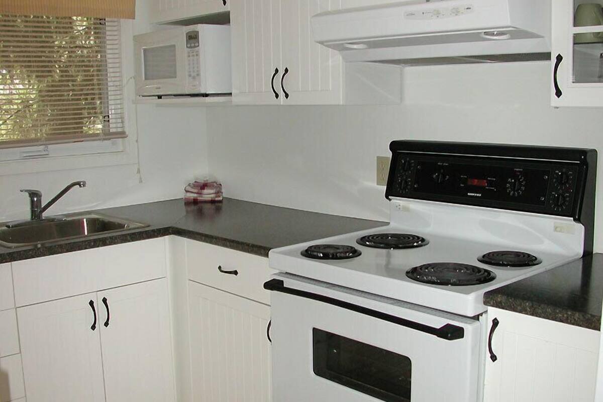A kitchen with white cabinets, a stove, a microwave, and a sink.