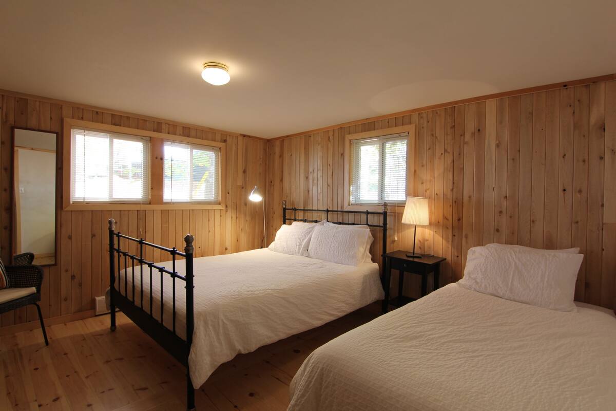 A bedroom with two beds, wooden walls, and a window.