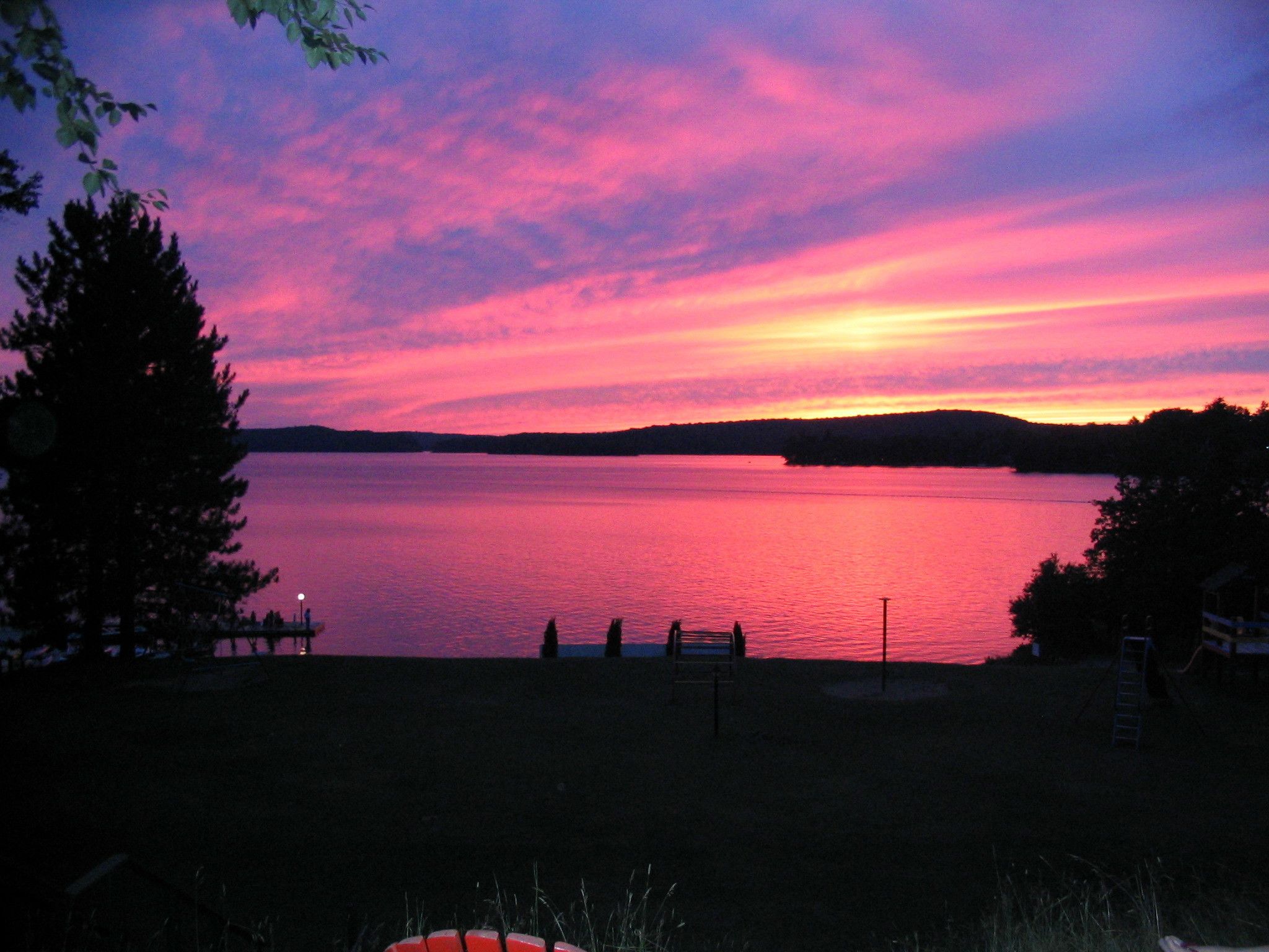 A lakeside view at sunset with a dock and a small building in the foreground.