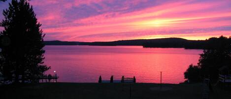 A lakeside view at sunset with a dock and a small building in the foreground.