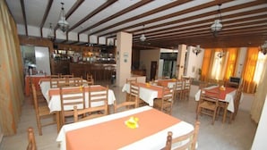 Un restaurant doté de nombreuses tables et chaises en bois, d’un bar et offrant une vue sur l’extérieur.