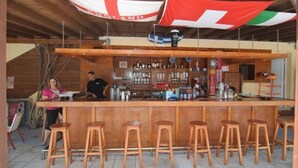 Un espace bar avec des tabourets en bois, un comptoir et des drapeaux suspendus au plafond.