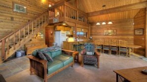Een houten cabin interieur met een trap, een eethoek en een woonkamer met een bank en stoelen.