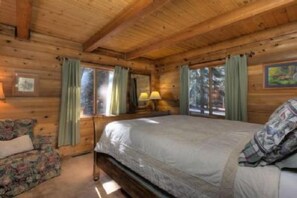 A wooden cabin room with a bed, a chair, and a window with curtains.