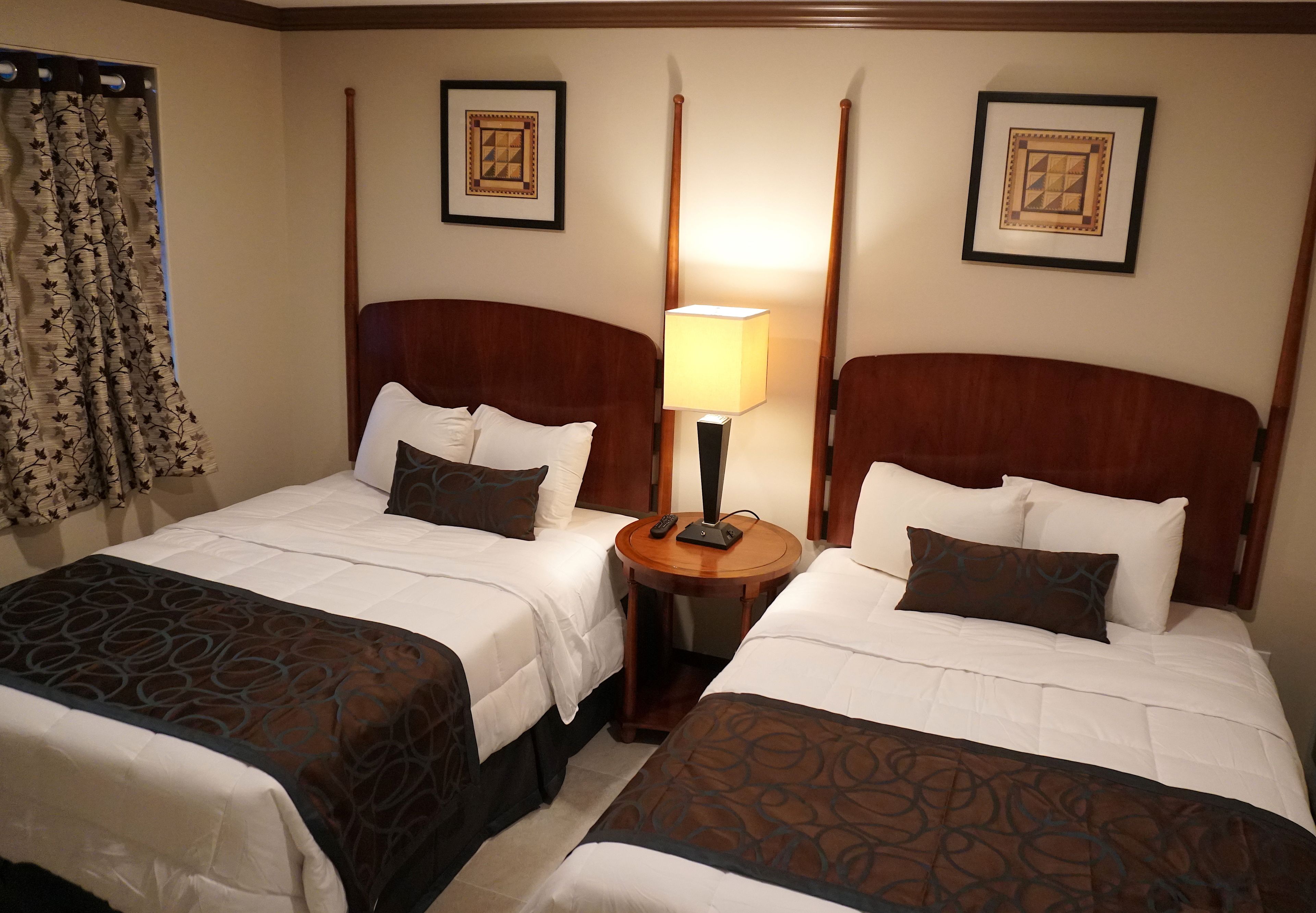 A hotel room with two beds, a nightstand with a lamp, and two framed pictures on the wall.