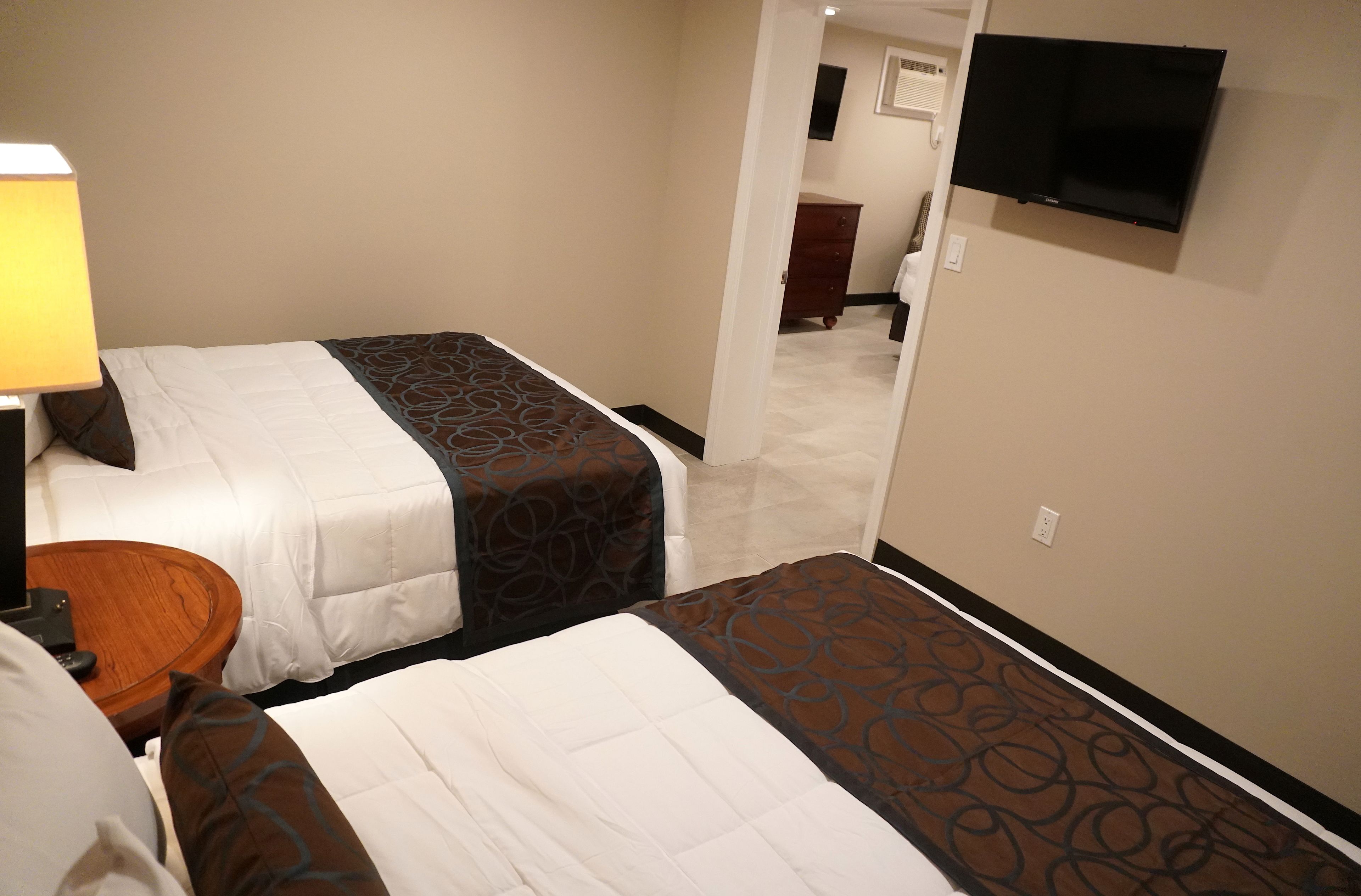 A hotel room with two beds, a TV mounted on the wall, and a wooden nightstand with a lamp.