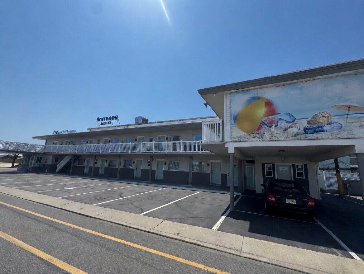 Een motel met een parkeerplaats, een muurschildering van strandtaferelen en een bord met de naam van het motel.