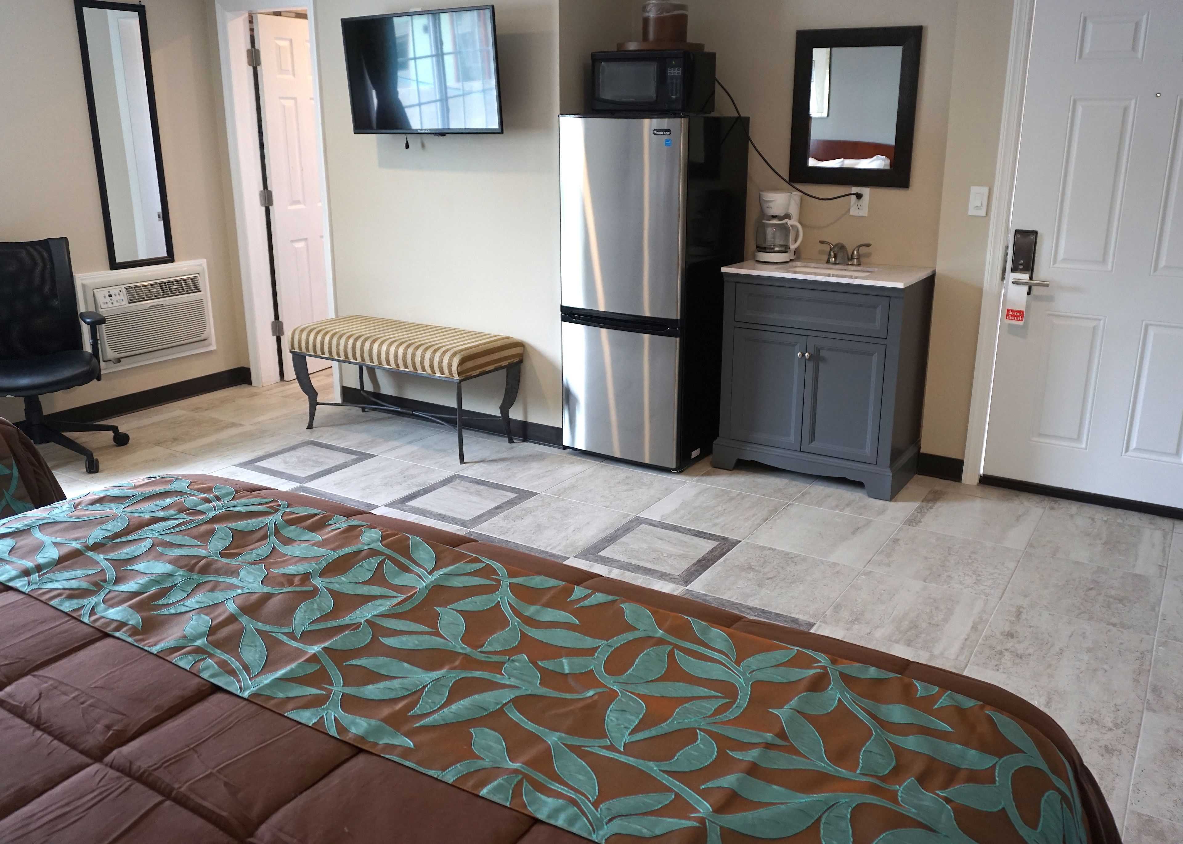 A hotel room with a bed, a bench, a refrigerator, a microwave, a coffee maker, and a cabinet.