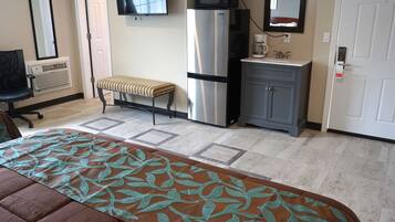 A hotel room with a bed, a bench, a refrigerator, a microwave, a coffee maker, and a cabinet.