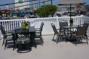 Un patio al aire libre con una mesa y sillas, una valla blanca y vistas a la calle y edificios al fondo.