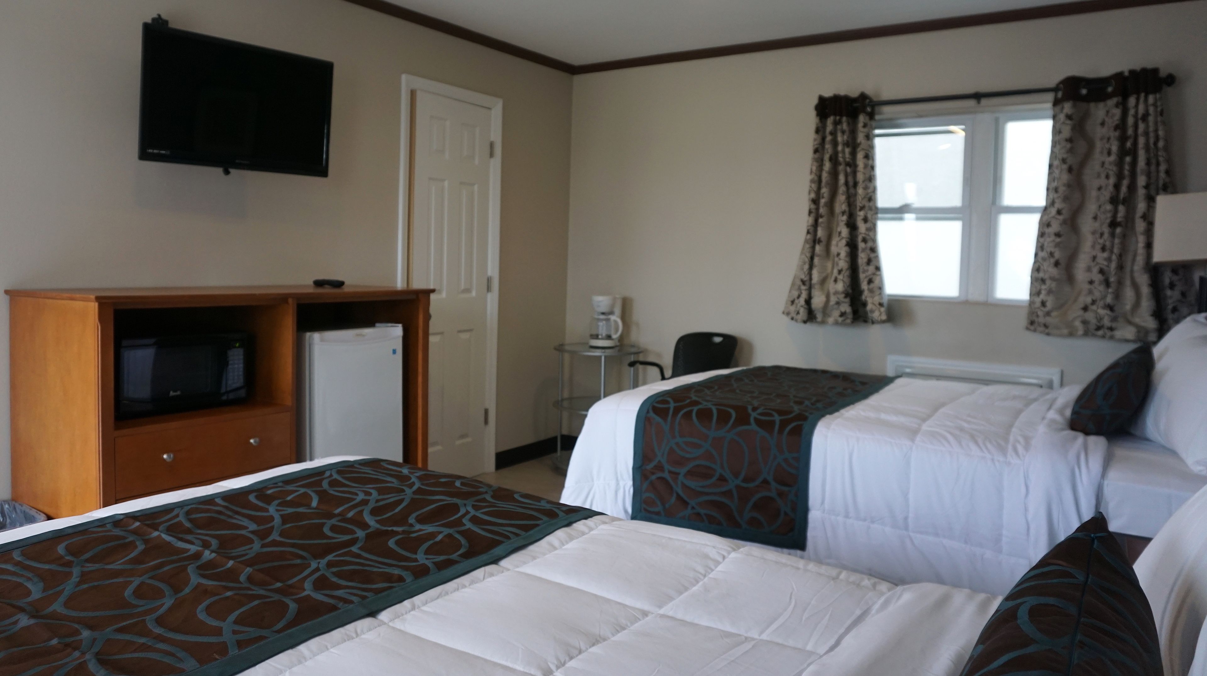 A hotel room with two beds, a television, a coffee maker, and a window with curtains.