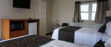 A hotel room with two beds, a television, a coffee maker, and a window with curtains.