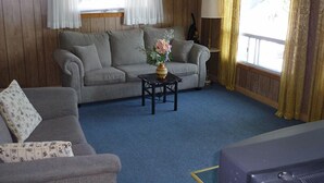 Un salon chaleureux avec un canapé gris, une petite table sur laquelle est posé un vase de fleurs et une lampe.