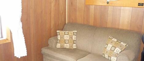 Un sofá beige con cojines estampados, un pez colgado en la pared y una ventana con cortina blanca.