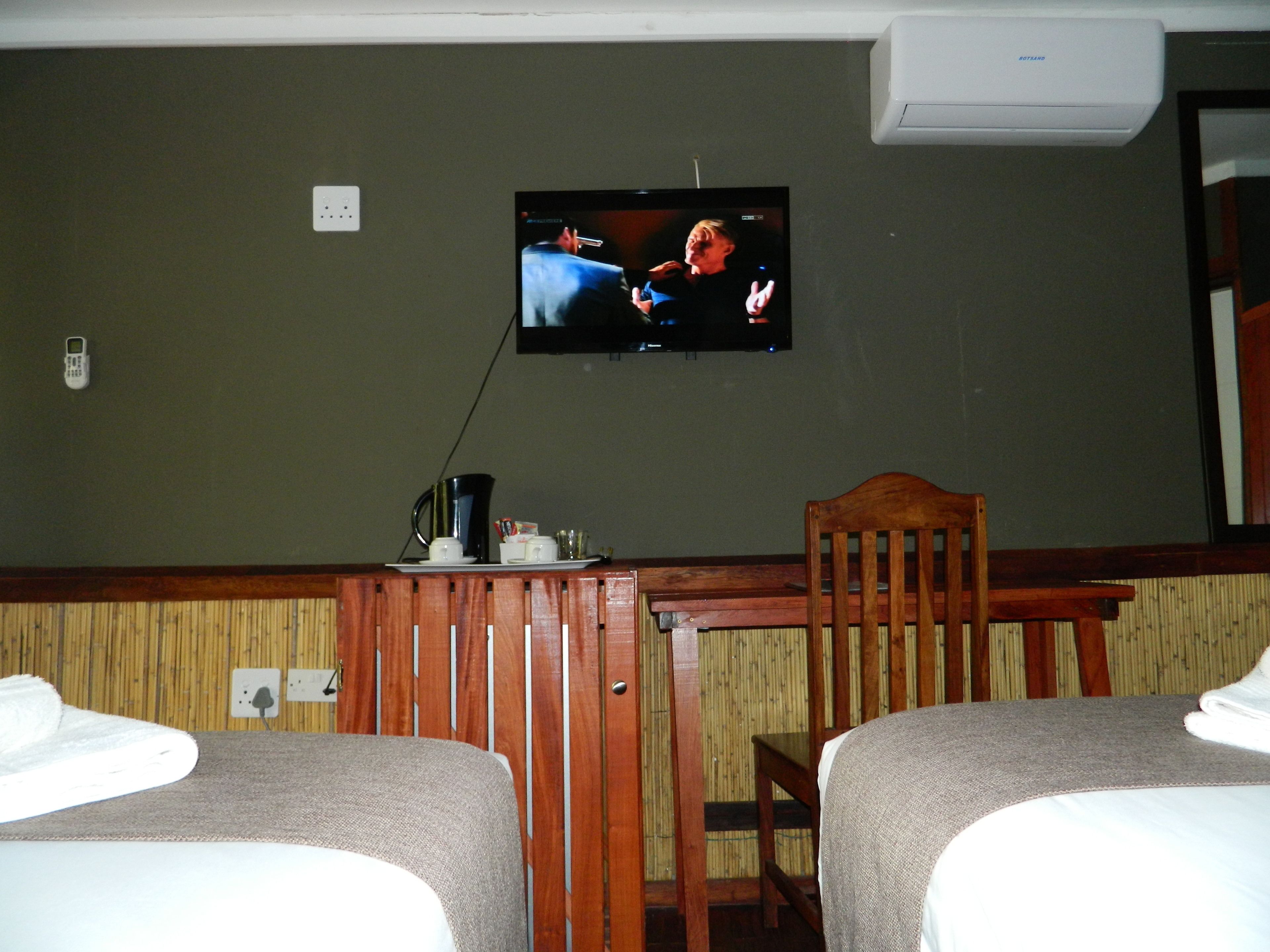 Habitación de hotel con dos camas, un televisor en la pared, una mesa de madera y una silla.