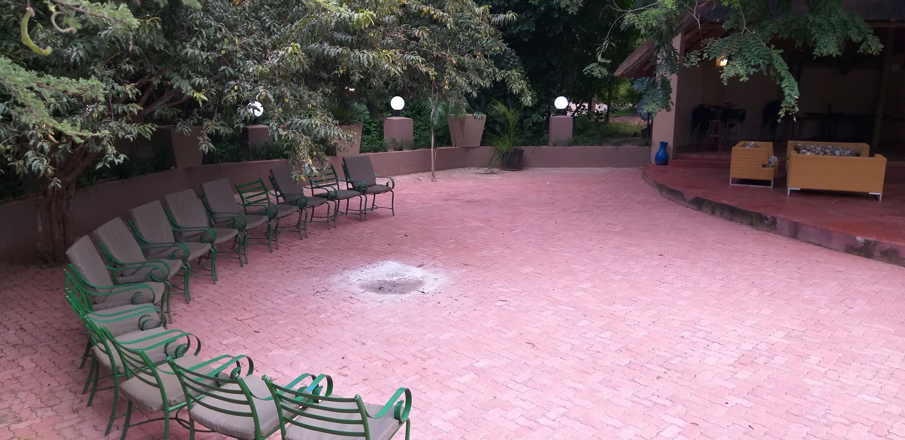 Un espace extérieur aménagé avec des chaises et des tables en métal vert, entouré de plantes en pot et d’arbres.