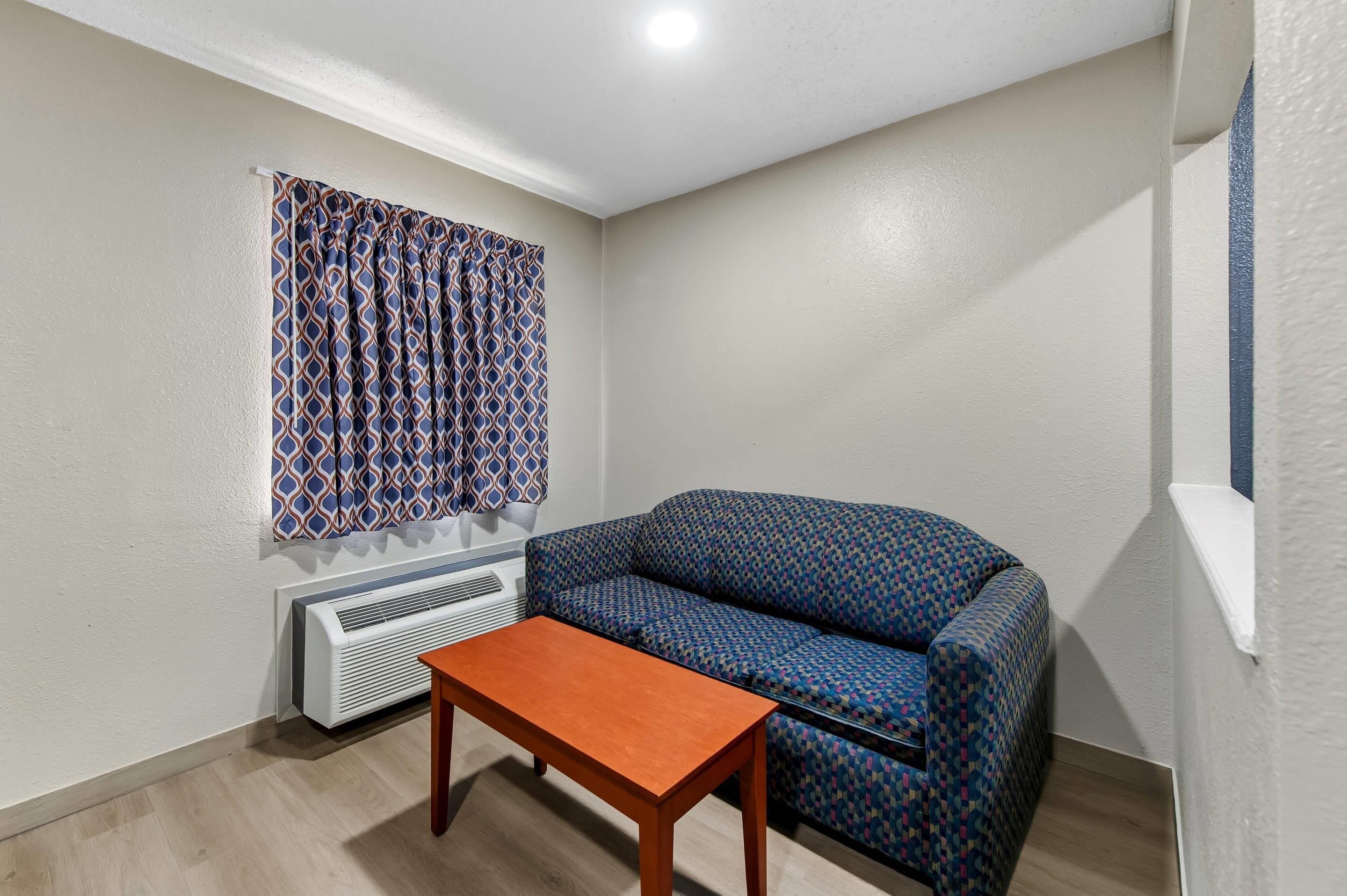 A small room with a patterned sofa, a wooden table, and a window with patterned curtains.