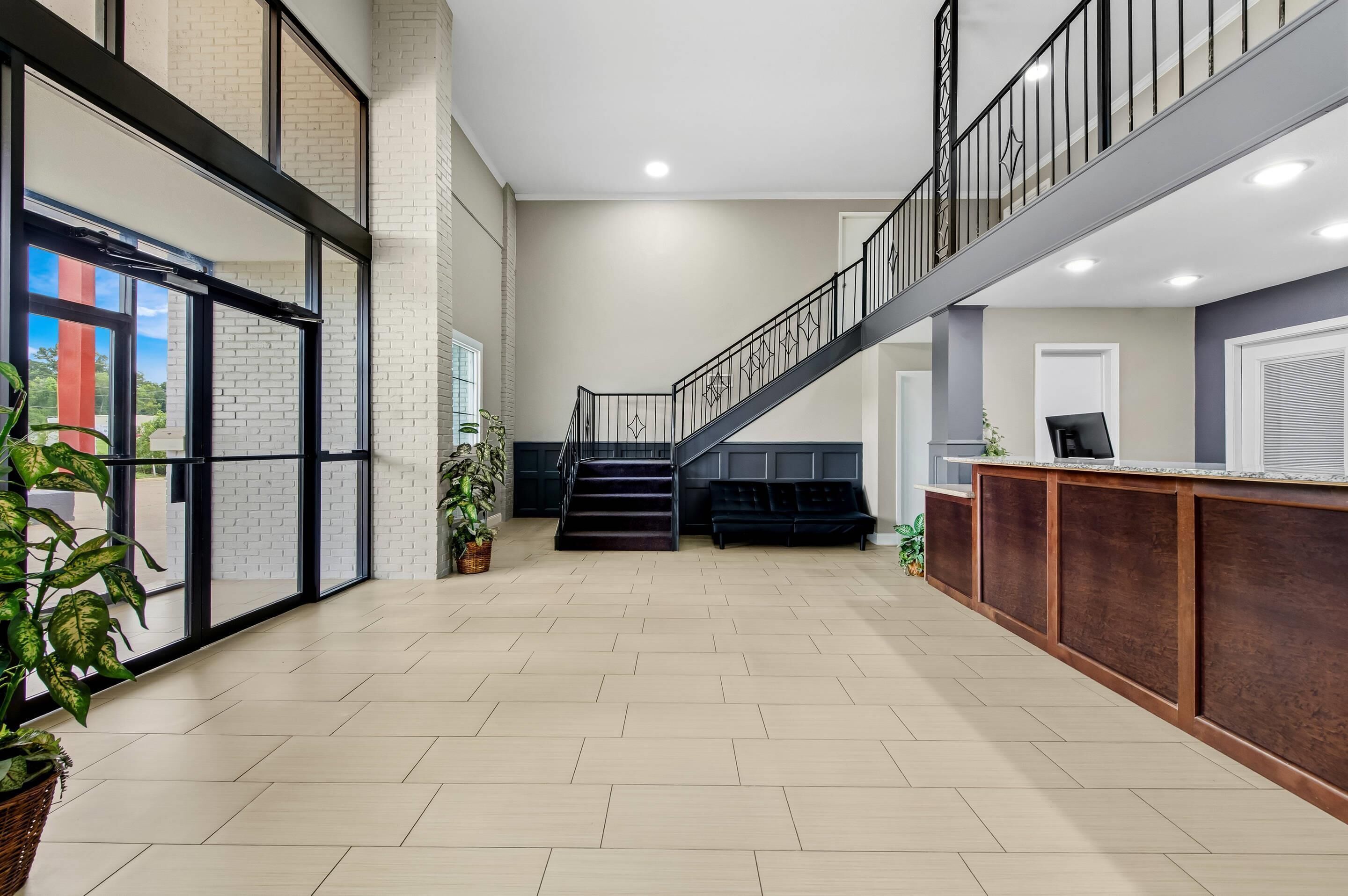 A spacious lobby with a staircase, a reception desk, and potted plants.