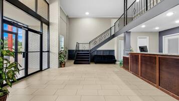 A spacious lobby with a staircase, a reception desk, and potted plants.