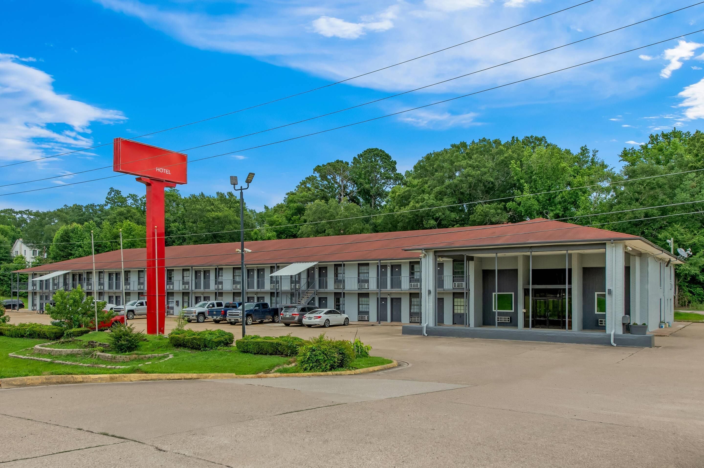 A motel with a red sign, multiple parking spaces, and a well-maintained lawn.
