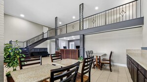 A spacious dining area with a high ceiling, a staircase, and a kitchen area with dark wooden cabinets.