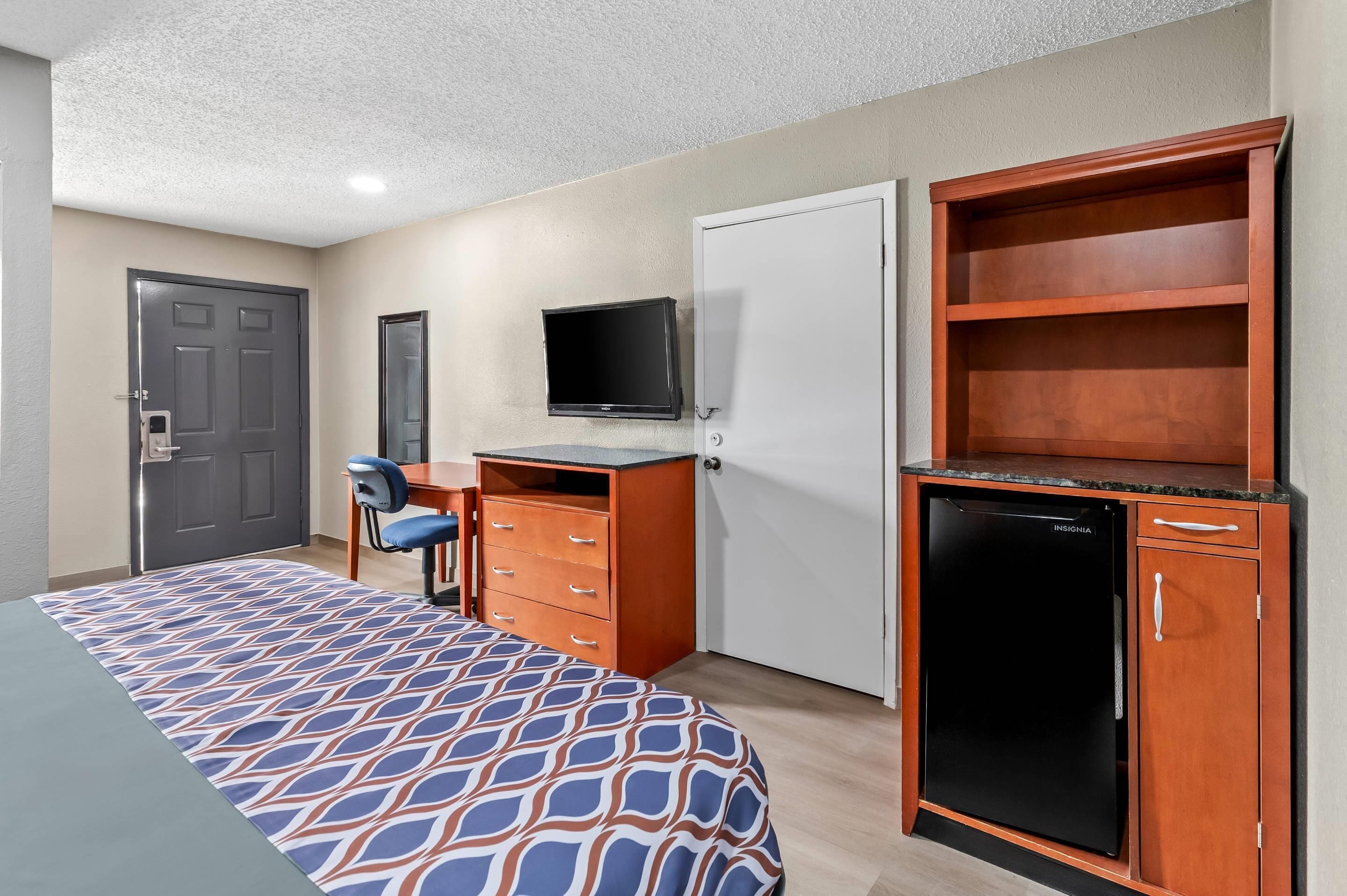 A hotel room with a bed, a desk with a computer, a television, and a minibar.