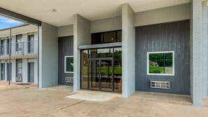 A building entrance with a glass door, a small window, and a concrete ground.