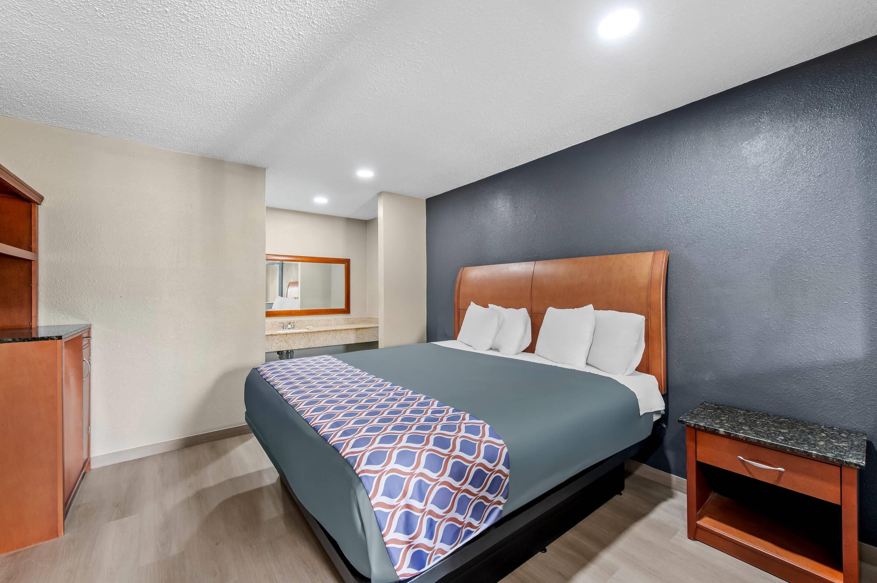 A hotel room with a bed, a nightstand, a wooden cabinet, and a mirror.