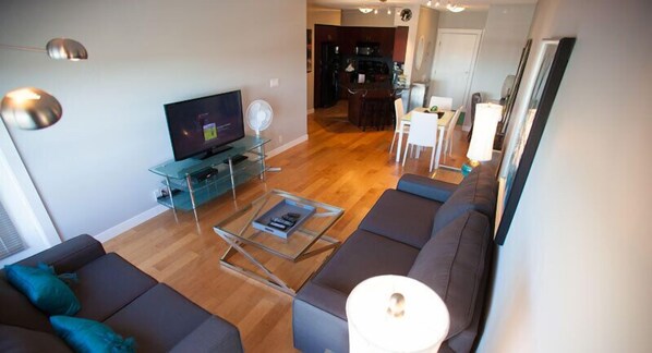 Una sala de estar moderna con televisor de pantalla plana, una mesa de centro de vidrio y sofás oscuros.