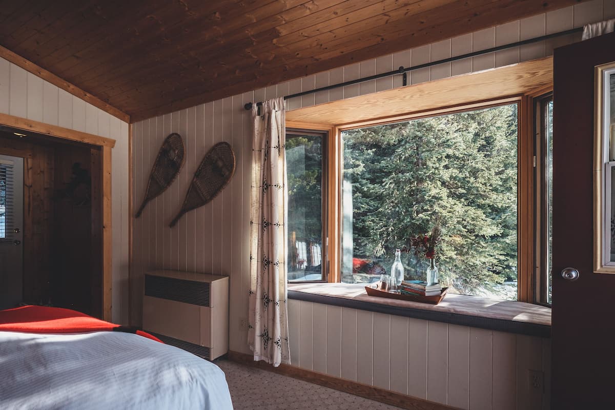 A bedroom with a bed, a window with a view of trees, a radiator, and a door.