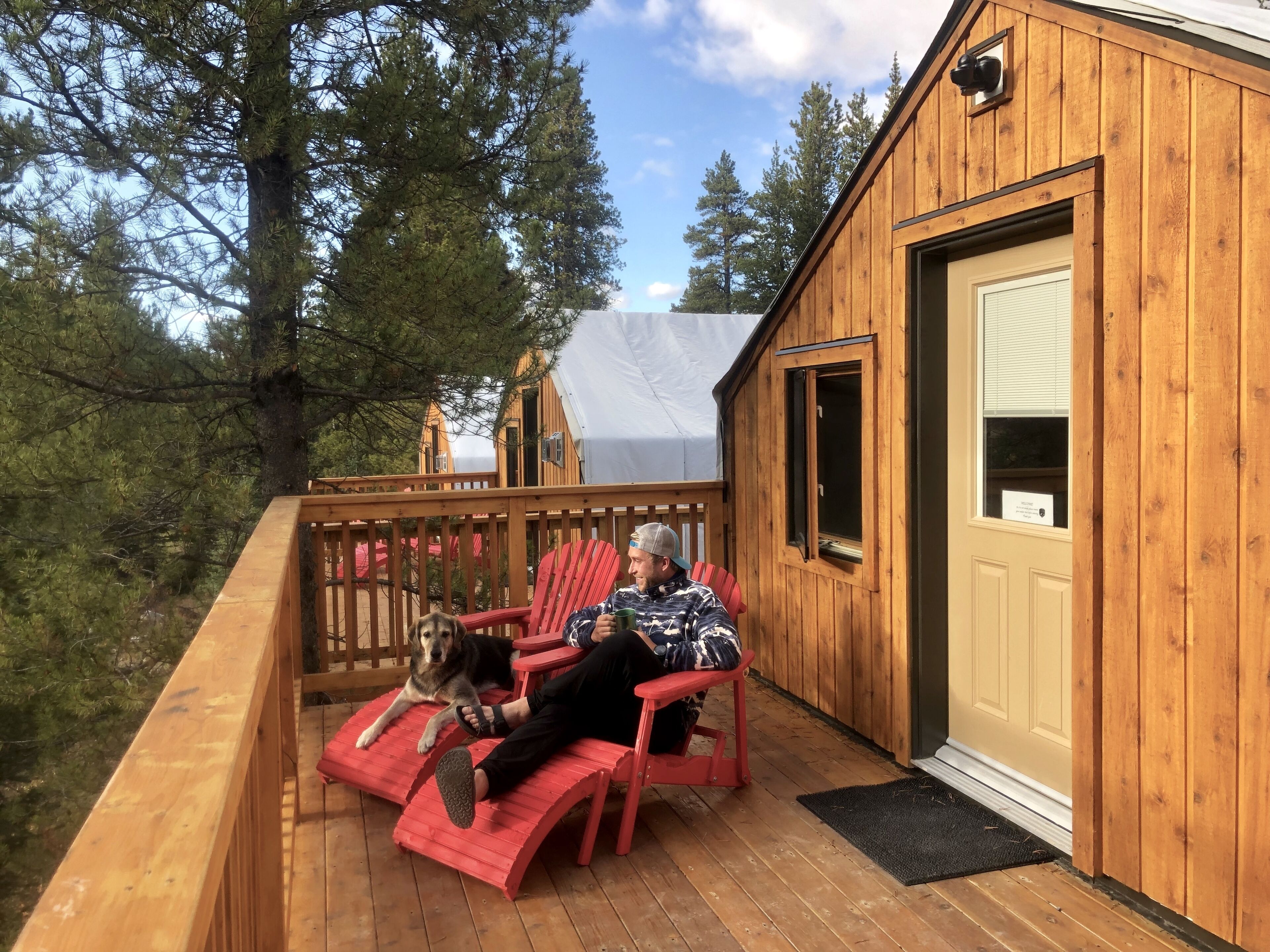 A wooden cabin with a deck, a red chair, and a dog.