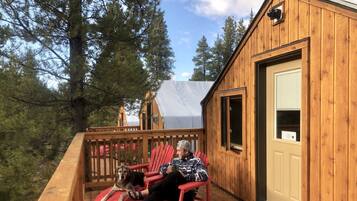 A wooden cabin with a deck, a red chair, and a dog.