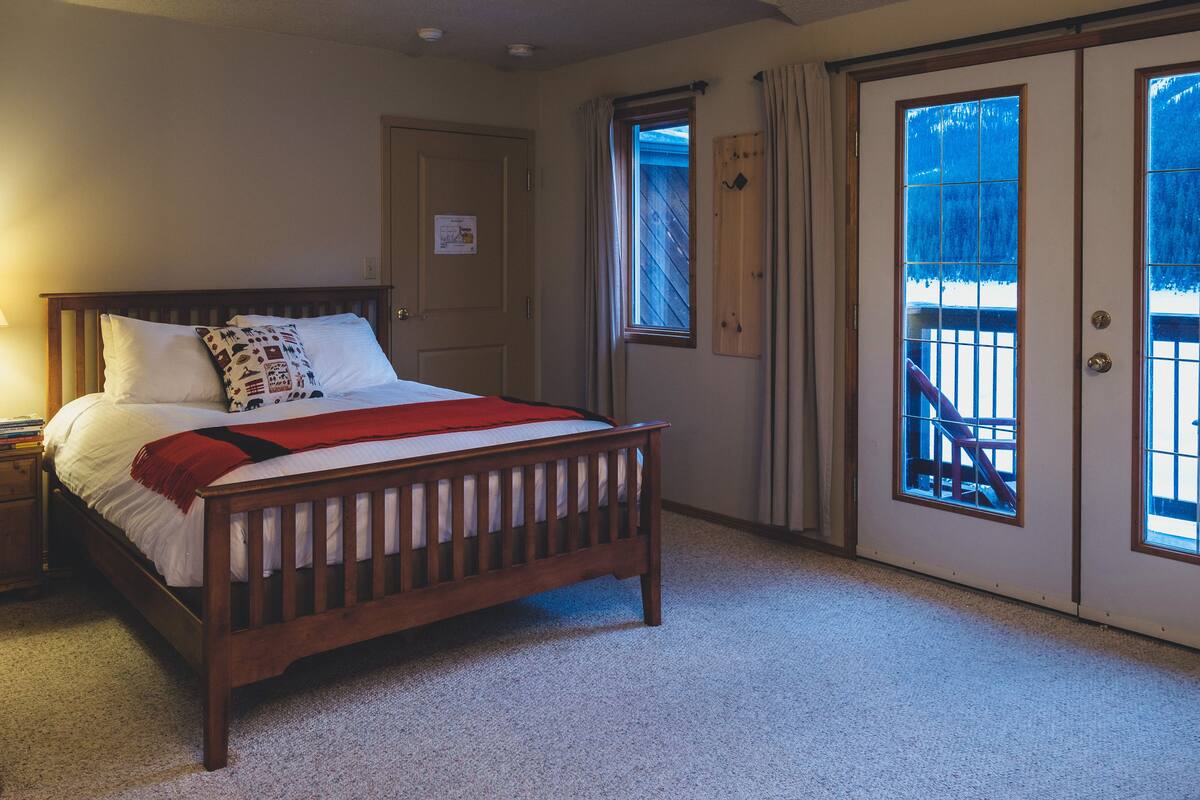 A bedroom with a wooden bed, a nightstand, a window with a view, and a door.