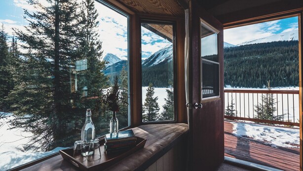 Una habitación con un banco de madera y una ventana que da a un paisaje nevado con árboles y montañas.