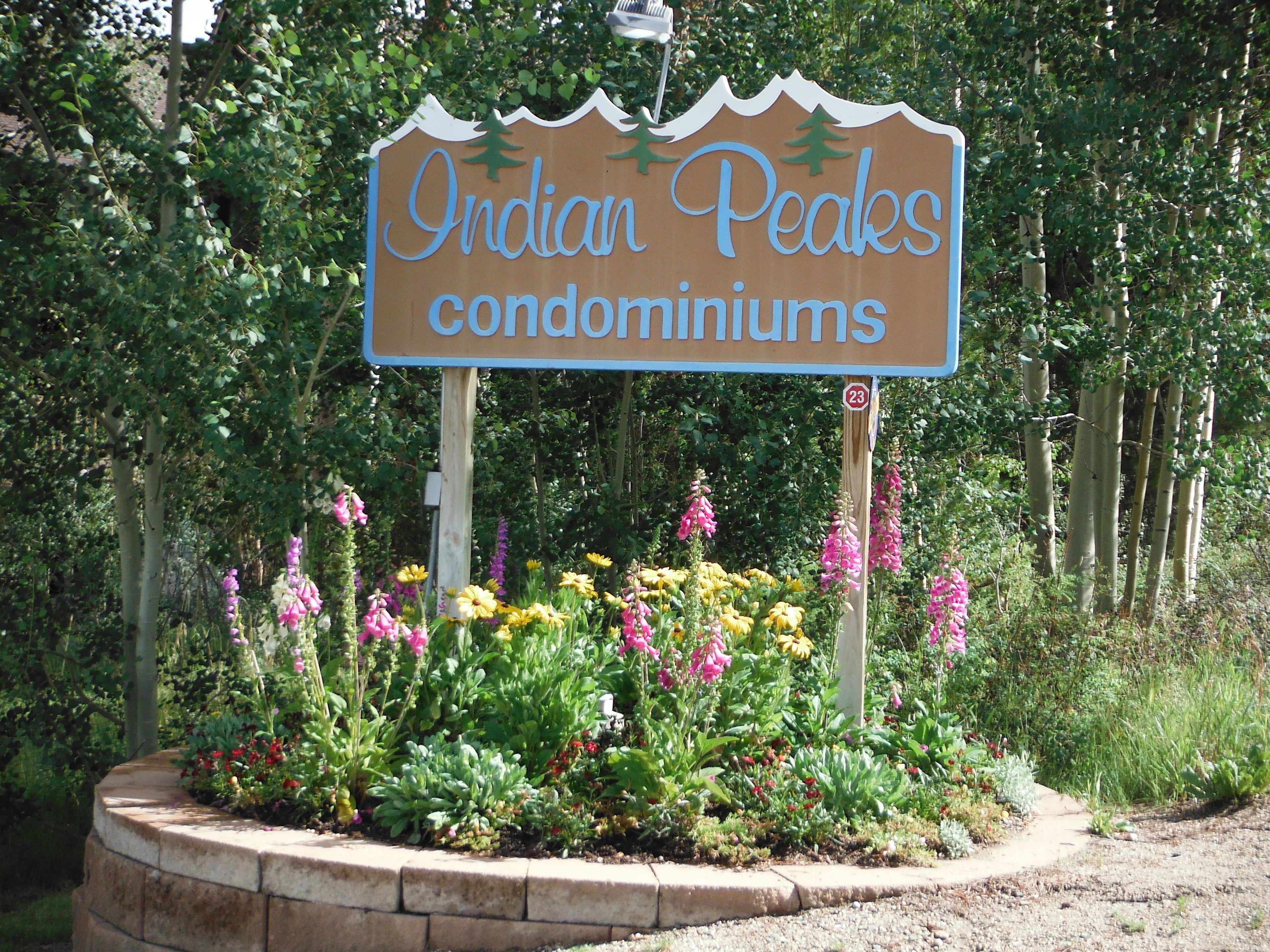 Segnaletica per i condomini Indian Peaks, immersi in un giardino curato con fiori vari.
